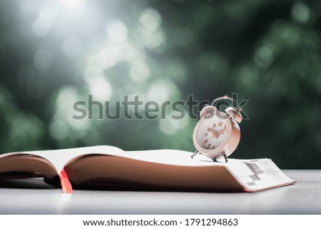 Alarm clock and book with beautiful nature background.