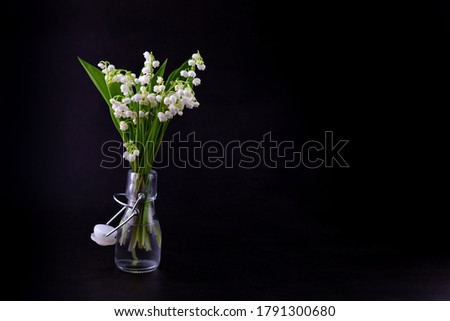 A bouquet of lilies of the valley on a black background with place for text. Delicate white spring flowers. Bouquet in a glass bottle. Copy space. Place for your text. 