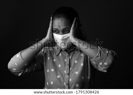 Black and white image of a woman wearing face mask with a troubled face in a dark background