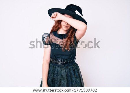 Young beautiful woman wearing witch halloween costume covering eyes with arm, looking serious and sad. sightless, hiding and rejection concept 