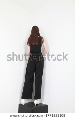 Backside view of a slim and slender tall girl in total black pants outfit, posing on a white wall background with black floor, Shooting for online store, promoting clothes