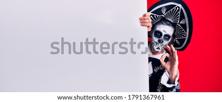 Young man wearing mexican day of the dead costume holding blank empty banner doing ok sign with fingers, smiling friendly gesturing excellent symbol 