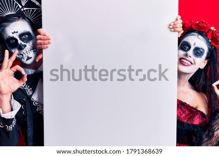 Young couple wearing mexican day of the dead costume holding blank empty banner doing ok sign with fingers, smiling friendly gesturing excellent symbol 