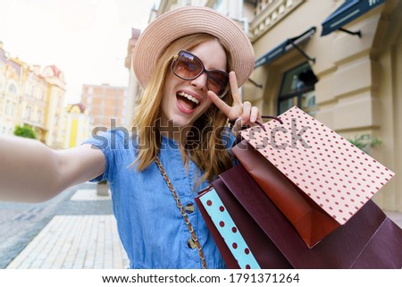 Young Woman with shopping bags making selfie walking in a city at summer day