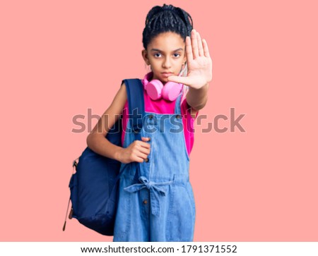 Cute african american girl holding student backpack using backpack with open hand doing stop sign with serious and confident expression, defense gesture 