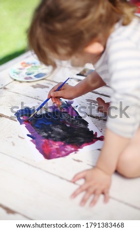 Little girl draws a colorful picture outside with watercolor paint on summer day. Creativity in childhood. Kindergarten activities for toddlers.  Preschooler learns art. 