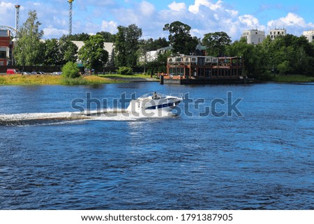 White boat sailing on the river against the background of a floating restaurant, trees and a blue sky with clouds. St. Petersburg.