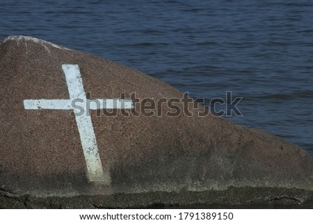 White cross painted on the rock in the sea. Close-up picture.