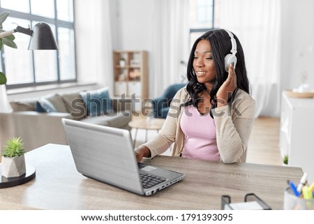 remote job, technology and people concept - happy smiling african american young woman in headphones with laptop computer working at home office