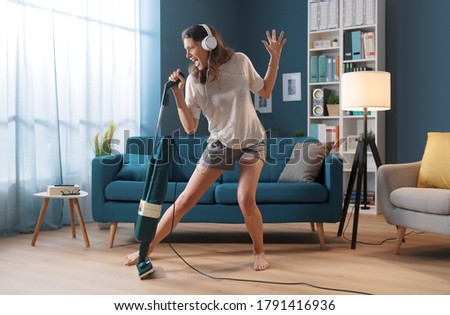Cheerful woman cleaning up her home and singing, she is using the vacuum cleaner as a microphone Royalty-Free Stock Photo #1791416936
