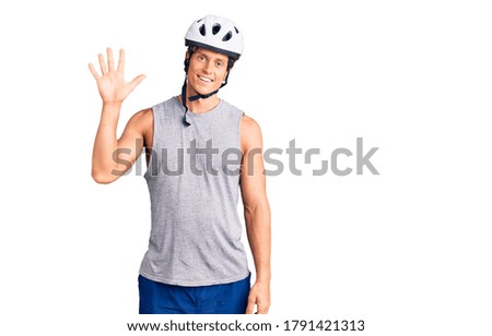 Young handsome man wearing bike helmet showing and pointing up with fingers number five while smiling confident and happy. 