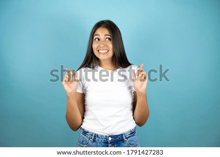 Young beautiful woman over isolated blue background gesturing finger crossed smiling with hope and looking side