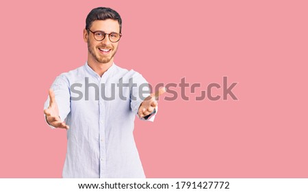 Handsome young man with bear wearing elegant business shirt and glasses smiling cheerful offering hands giving assistance and acceptance. 