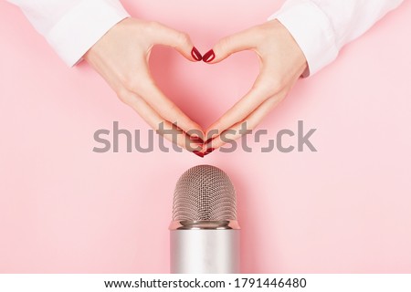 Woman hands in a heart shape and a microphone on pink background.