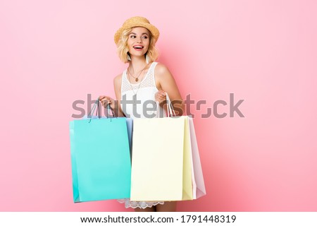 excited woman in straw hat and white dress holding shopping bags on pink