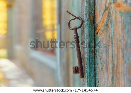 An old iron retro key hanging on a nail against the wall of a rustic wooden house, the concept of a secret, inheritance, opportunity.