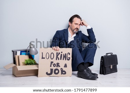 Full length photo of  aged guy jobless man hold placard need work sit floor briefcase belongings box stuff lost everything wear suit shoes isolated grey background Royalty-Free Stock Photo #1791477899