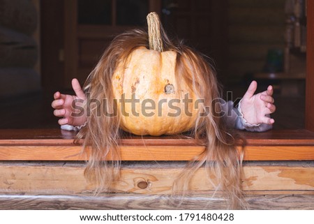 On the threshold lies a large orange pumpkin with hair and arms, stretching out his arms forward. Halloween, autumn holiday, tradition. Spooky scary fairytale character. Copy space.