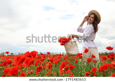 Woman holding handbag with poppy flowers in beautiful field