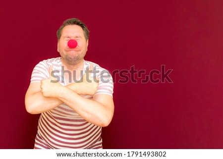 The happy surprised charming trendy and smiling man shows thumb up on red or burgundy wall.Red nose day or april fools day. The clown, fun, party, celebration, funny, joy, holiday, humor concept