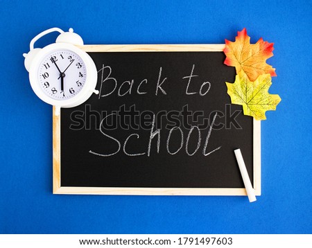 Blackboard, white chalk, white alarm clock, colorful autumn leaves. The inscription on the Board. The concept of going back to school. Flatley