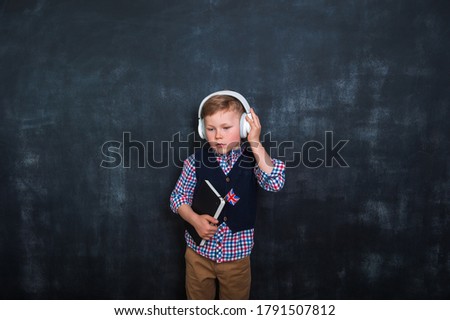 Kid in uniform and headphones holding a flag of United Kingdom and book in hands. Great Britain flag. British flag. Education and learn English. International language school concept. Innovation