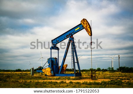 Oil Rig Pumping Fracked Natural Gas and Fossil fuel carbon out of the ground in West Texas with Wind Turbines far in the distance a energy landscape Royalty-Free Stock Photo #1791522053
