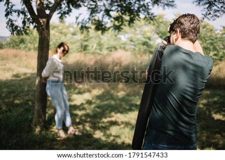 Photographer with professional camera taking photos of blurred female model in forest.