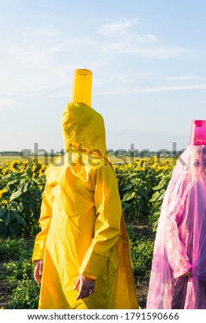 two figures of a man and a woman in yellow and pink raincoats in the background a field of sunflowers. bright colors, art photo