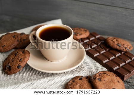 Coffee cup with cookies and chocolate on wooden table background. Mug of black coffee with chocolate cookies. Fresh coffee beans.