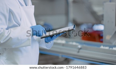 Quality Supervisor or Food Technician is Inspecting the Automated Production at a Food Factory. Close Up Shot of Employee Using Tablet Computer for Work. He Types In Data While Wearing Latex Gloves. Royalty-Free Stock Photo #1791646883