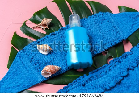 Blue bikini with sunblock spray bottle and monstera leaf and seashells
