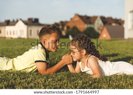 young brother and sister lying on the grass are engaged in arm wrestling.