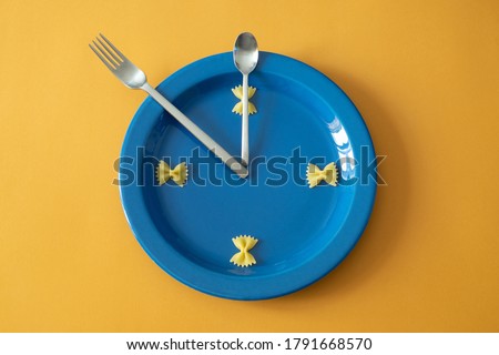 A creative clock composed of a plate on a yellow background, four butterflies of raw dough mark the hours, the cutlery symbolize the hands. Royalty-Free Stock Photo #1791668570