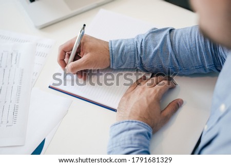 Man holding pen pencil in hand filling writing taking notes into notes starting new chapter businessman entrepreneur clean start new fresh idea top down view over the shoulder