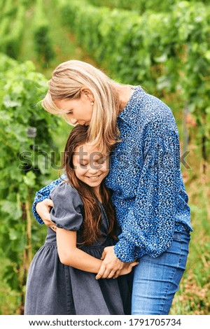 Outdoor portrait of lovely daughter and mother hugging each other, playing in green garden, happy parenting