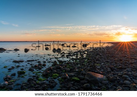Scenic sunset with sun star over stone beach in South part of Sweden. Nature background.