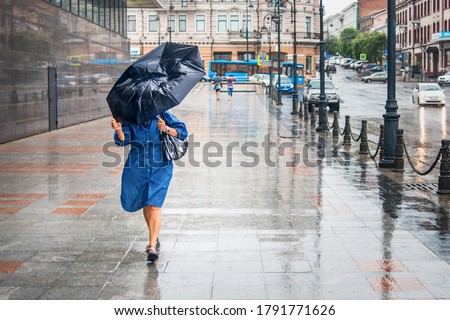 Woman in bad rainy weather walks down the street and tries to keep the umbrella from the strong wind. City landscape in rainy weather. City scenes in the rain.