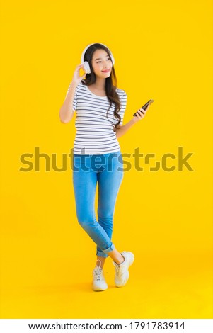 Portrait beautiful young asian woman use smart mobile phone with headphone for listen music on yellow isolated background