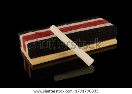 An isolated over black reflective surface image of a wooden chalkboard eraser and a new stick to write with.
