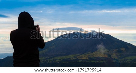View of a beautiful sunrise from a Volcano with very colorful clouds and a man taking his fumography