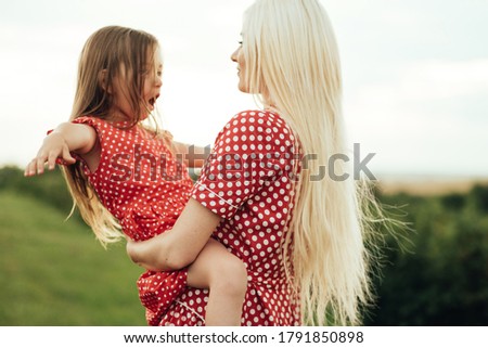 Young Mom with her Little Daughter Dressed Alike in Red Polka Dot Dress, Having Fun Time in Field Outside the City, Motherhood and Childhood Concept