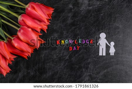 Knowledge day. Red tulips with paper figures father and daughter on chalk board. Top view. Back to school