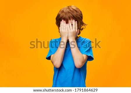 The boy covered his face with his hands red hair tears blue t-shirt 