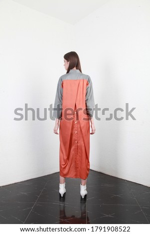 Backside view of a slim and slender tall girl in stylish outfit, posing on a white wall background with black floor, Shooting for online store, promoting designer clothes. Model wearing trendy dress