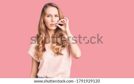 Young beautiful caucasian woman with blond hair wearing casual clothes mouth and lips shut as zip with fingers. secret and silent, taboo talking 