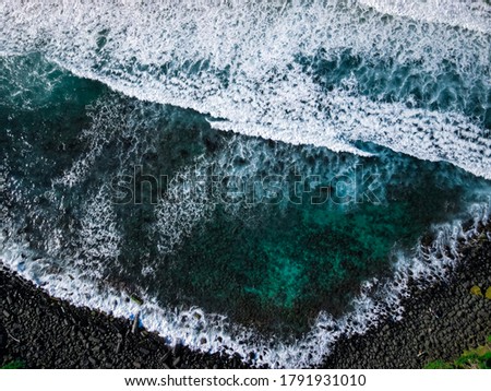 High Definition Aerial Photography of Ocean Waves on a Rocky Shoreline with Green Rainforest Trees in Background.  Cold Winter Blue Green Water and Stone Beach with Breaking Surf
