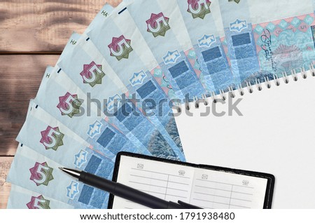 5 Ukrainian hryvnias bills fan and notepad with contact book and black pen. Concept of financial planning and business strategy