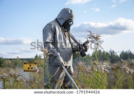 A military man dressed as chemical troops is examining the radioactive territory; a radio station sign is installed in the field.  Smoke and fog. Royalty-Free Stock Photo #1791944426