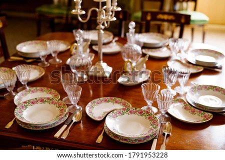 Festive table setting with plates, spoons, knives, glasses, decanters and a candlestick in the center on a wooden table.
